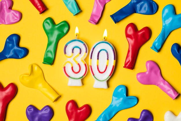 Number 30 candle with party balloons on a bright yellow background