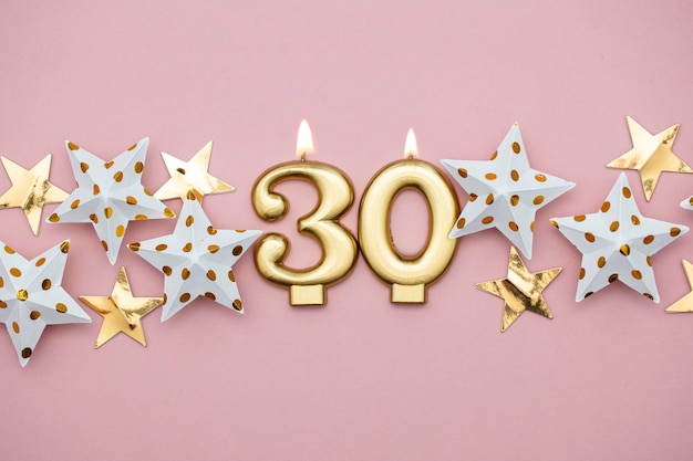 Number 30 gold candle and stars on a pastel pink background