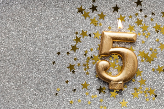 Number 5 gold celebration candle on star and glitter background