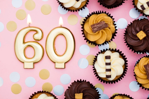 Number 60 gold candle with cupcakes against a pastel pink background