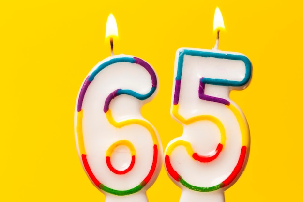 Number 65 birthday celebration candle against a bright yellow background