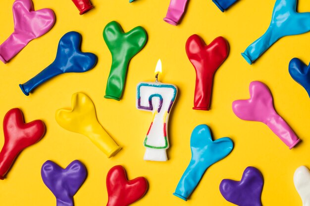 Number 7 candle with party balloons on a bright yellow background