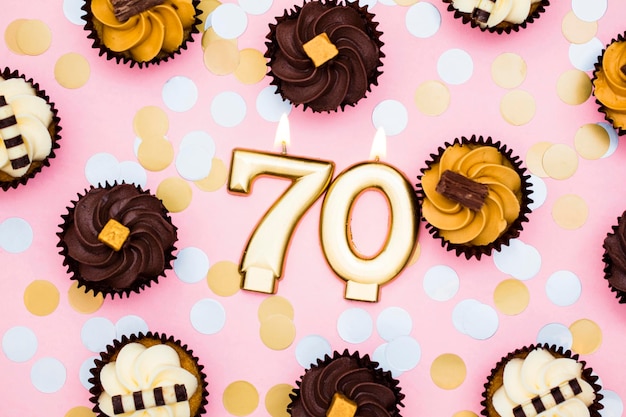 Number 70 gold candle with cupcakes against a pastel pink background