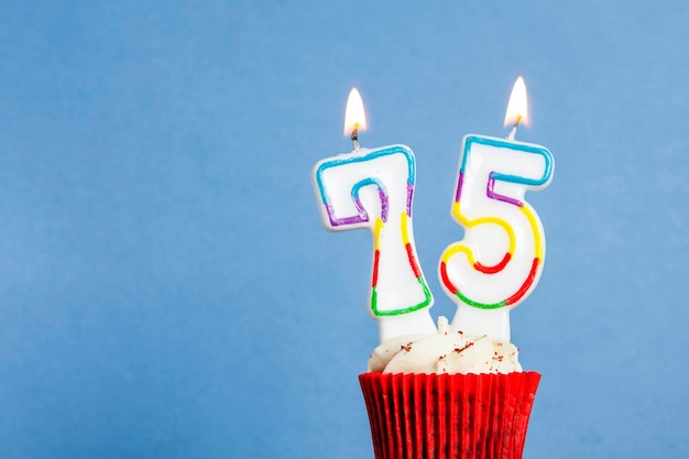 Number 75 birthday candle in a cupcake against a blue background