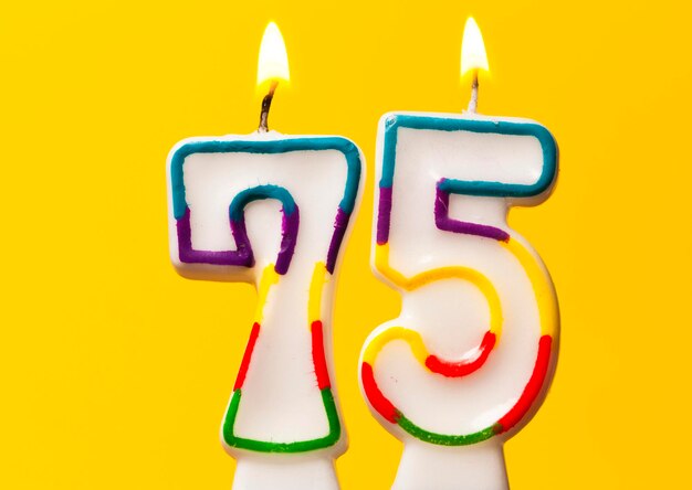 Number 75 birthday celebration candle against a bright yellow background