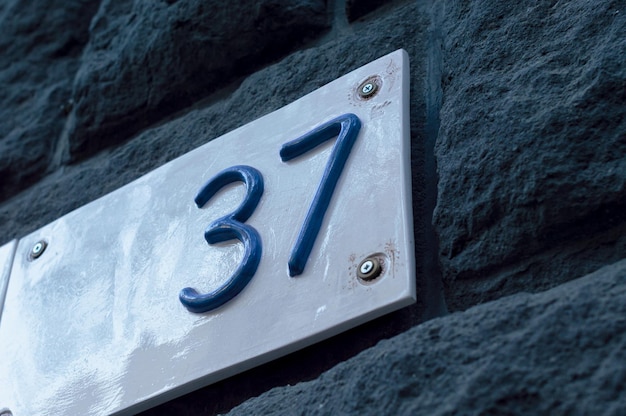 Фото Белая керамическая номерная табличка с синими цифрами на фоне каменных кирпичей