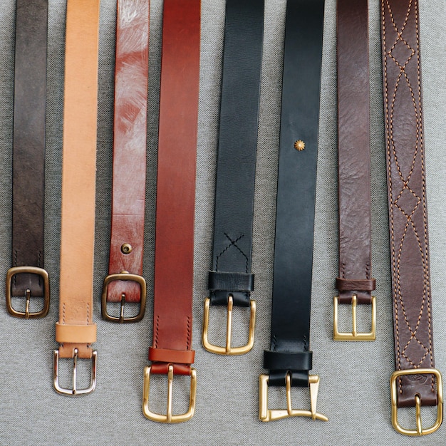 A number of classical faux leather belts lined up on a gray fabric surface