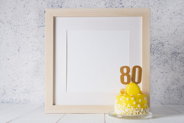 The number Eighty on the yellow cake next to the white frame mockup with copy space