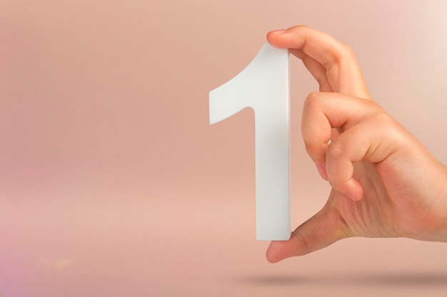 Number one in hand a hand holds a white number one on a red background with copy space concept with