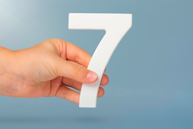 Number seven in hand hand holding white number on blue background with copy space concept with numbe