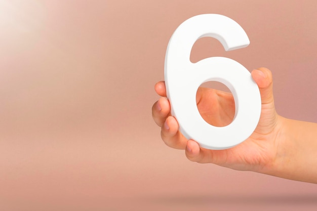 Number six in hand a hand holds a white number on a red background with copy space concept with numb