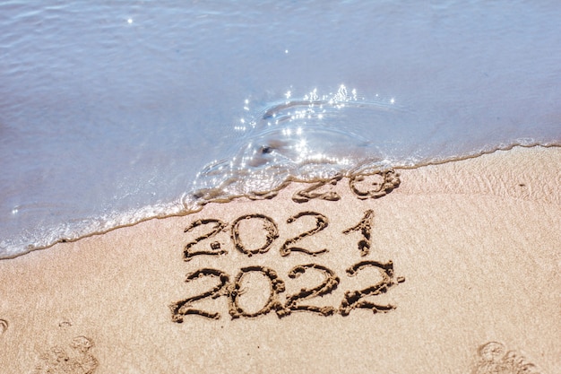 The numbers 2021, 2022 are drawn on the sand and washed away by the wave, the symbol of the new year, the change of the year, the calendar