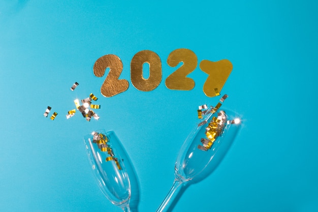 Numbers 2021 on a blue background with glasses of champagne and candy