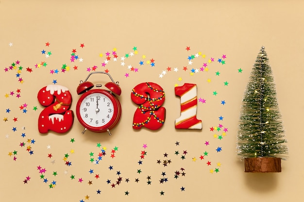 Numbers 2021 made from gingerbread cookies in multi-colored glaze on a beige background. Red alarm clock, multi-colored stars and a Christmas tree. New year 2021, Christmas holiday