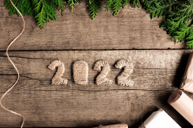 Numbers 2022 on an old brown wooden table with gifts and green branches top view