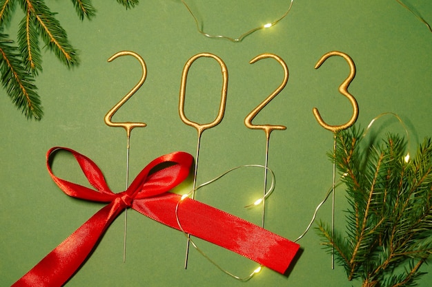 Numbers 2023 laid out from sparklers lie on green isolated background with fir branches and red ribbon The concept of the change of the year and New Year holidays