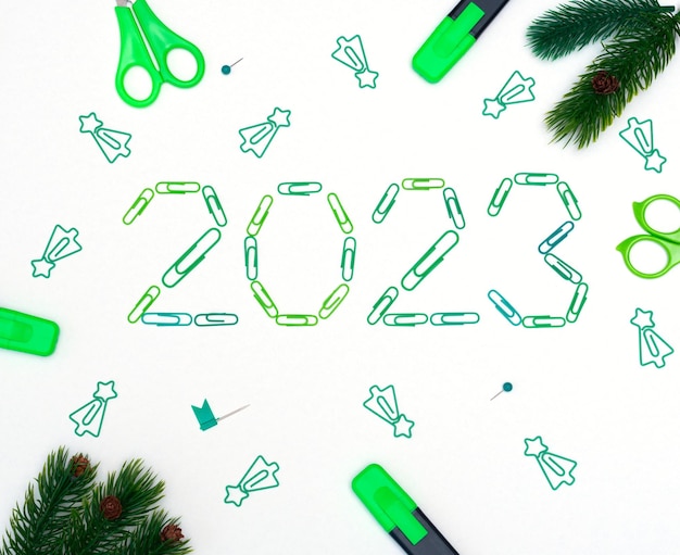 Numbers 2023 made of green clips with office supplies and Christmas decorative items on white background Xmas or New Year flat lay Festive winter composition Office holiday celebration concept