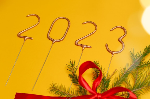 Numbers 2023 on yellow isolated background with red ribbon lanterns and pine branch Design for your postcard