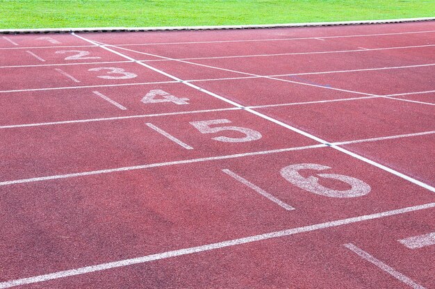 Начальная точка чисел на красной беговой дорожкебеговая дорожка и зеленая траваПрямая легкая атлетика Беговая дорожка на спортивном стадионе