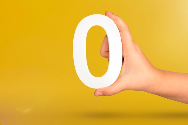 손에 숫자 0은 복사 공간 0 co가 있는 노란색 배경에 흰색 숫자 0을 보유하고 있습니다.
