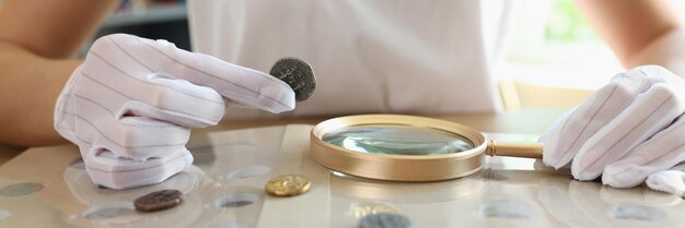 Numismatist in witte handschoenen onderzoekt oude munten collectie aan tafel close-up van vrouw met