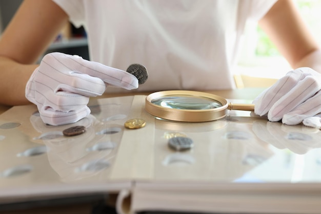 Numismatist in white gloves examines ancient coins collection at table