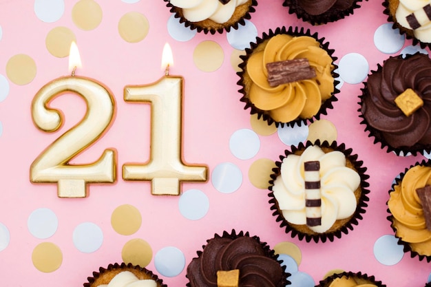 Nummer 21 gouden kaars met cupcakes tegen een pastelroze achtergrond