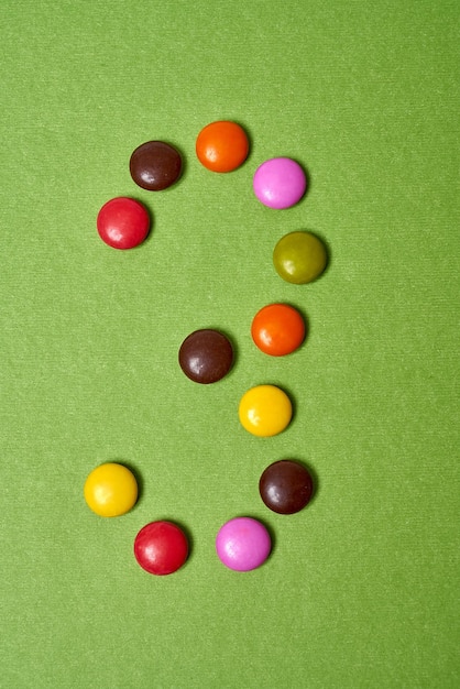 Nummer 3 geschreven met gekleurde ronde chocoladesuikergoed op groene achtergrond.