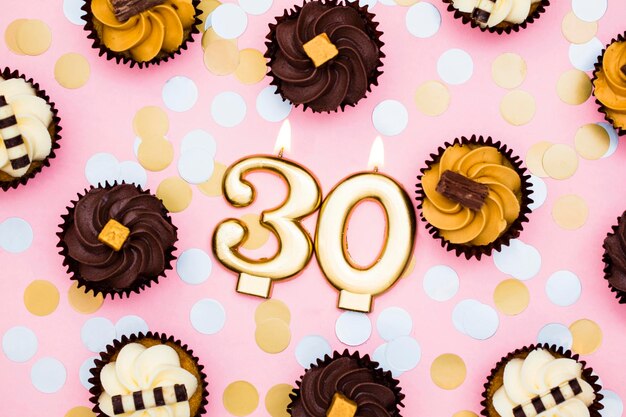 Nummer 30 gouden kaars met cupcakes tegen een pastelroze achtergrond