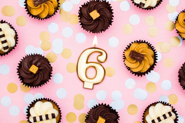 Nummer 6 gouden kaars met cupcakes tegen een pastelroze achtergrond