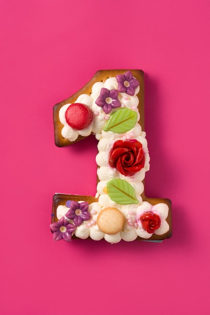 Nummer één cake versierd met bloemen en koekjes op roze oppervlak.