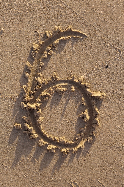 Nummer zes geschreven op een zandstrand. Handgeschreven karakters collectie.