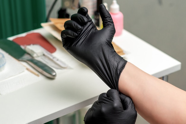 Nurse or beautician puts on medical latex black gloves.