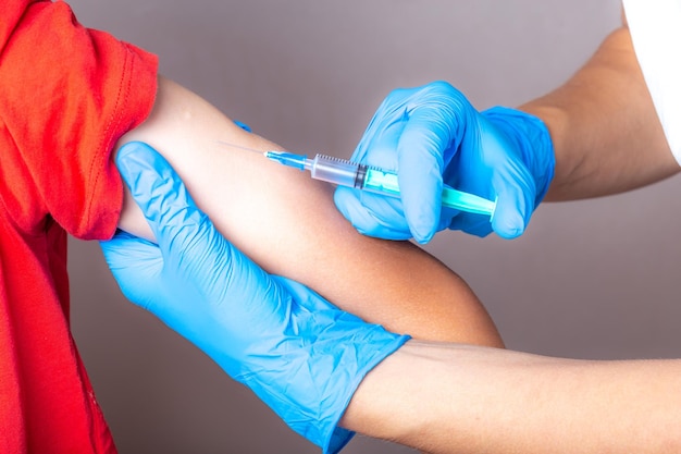 A nurse in blue gloves injects a vaccine through a syringe into the child's shoulder