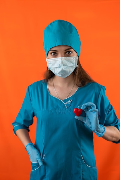 Медсестра в синей униформе с перчатками в маске держит маленькое красное сердце в операционной больнице
