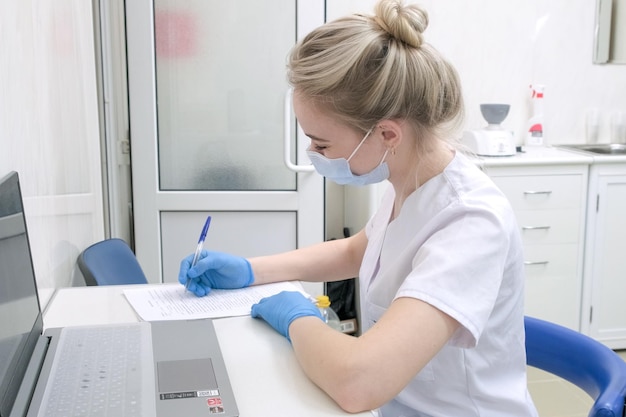 Nurse dentist assistant or female doctor in white uniform sits at desk in clinic or hospital