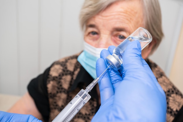 Nurse dials vaccine from ampoule close up on grandmother's background Vaccination of elderly people