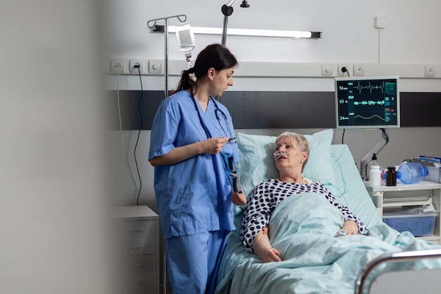 nurse discussing with elderly patient laying in hospital bed during visit about chest x-ray