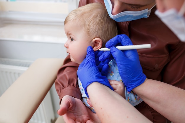 A nurse doctor pierces the ears of a little girl eight months old. Beauty for young children