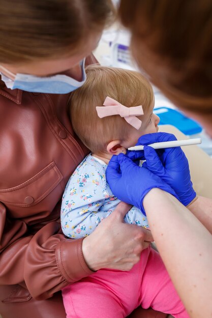 看護師の医者が生後8ヶ月の少女の耳を刺します。幼児のための美しさ