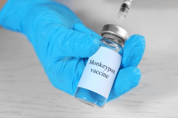 Nurse filling syringe with monkeypox vaccine from vial at white wooden table closeup