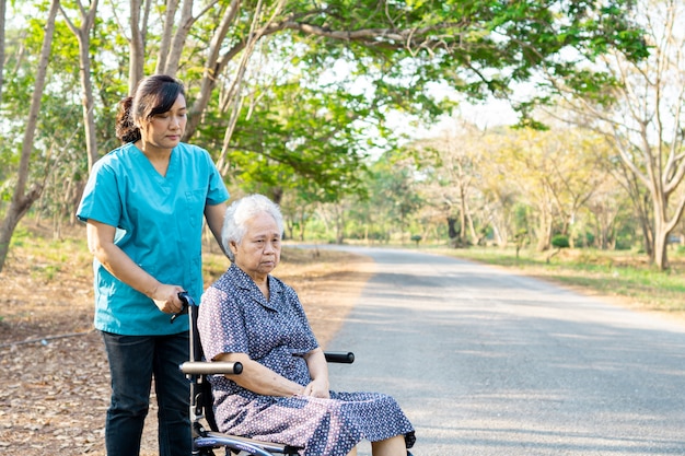 Nurse help and care Asian senior woman patient sitting on wheelchair at park.