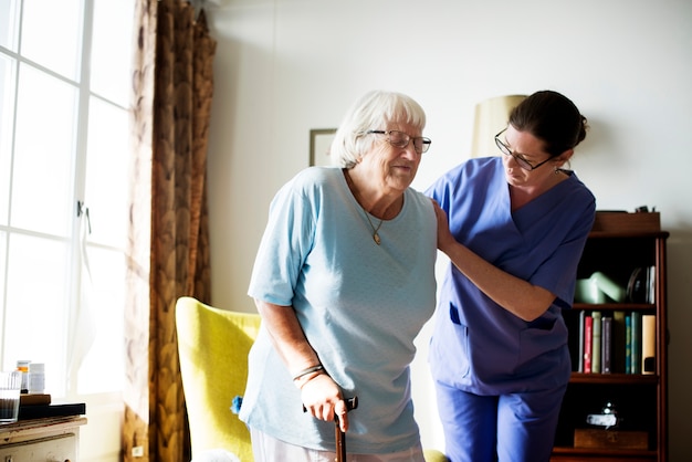Медсестра помогает старшей женщине встать