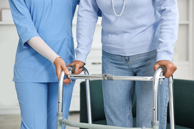 nurse helping senior woman with walking frame indoors closeup