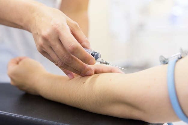 Nurse hitting injection on left arm of patient in hospital room