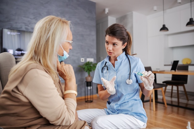 Nurse holding thermometer and giving advices to and old woman while sitting at home.