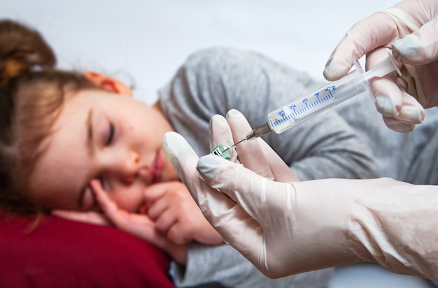 The nurse holds an injection syringe for little girl. A doctor in medical gloves prepares a syringe.