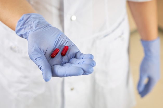 Nurse holds two red pills in her palm as a cure for the virus