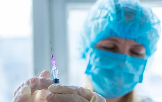 A nurse is holding a syringe with a vaccine on a light background