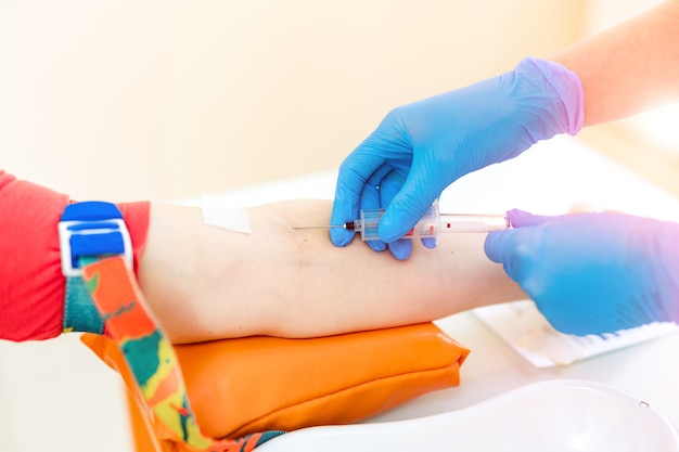 看護師は病院の患者の腕に針注射器を刺しています。研究室で血液検査のための血液サンプルを採取する青い滅菌手袋の女性の手。閉じる。